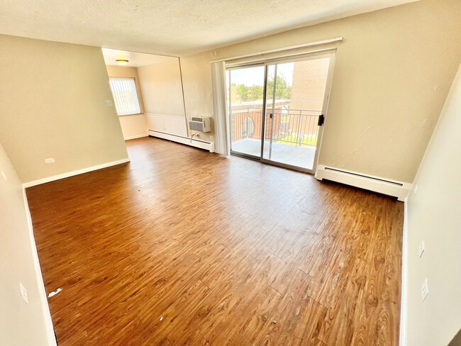 Bright and inviting living area with elegant wood flooring, opening to a sunny balcony through sliding glass doors. - Bonneville Apts