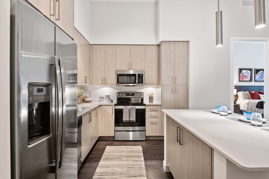 Kitchen with oak cabinetry, undercabinet lighting, white quartz countertops, stainless steel appliances, and hard-surface vinyl plank flooring - Avalon Fort Lauderdale