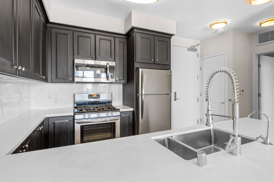 Kitchens with dark cabinetry, white quartz countertops, white tile backsplash, stainless steel appliances, and hard surface flooring - AVA Balboa Park