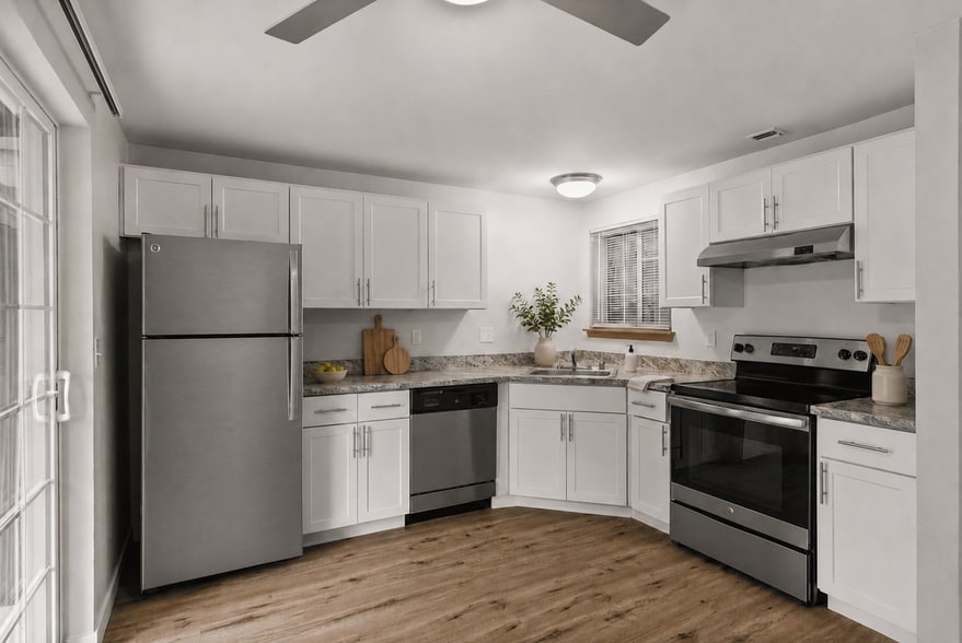 Staged apartment kitchen with white cabinetry, stainless-steel appliances, wood-look flooring, greenery, and modern countertop décor. - Stonegate Apartments