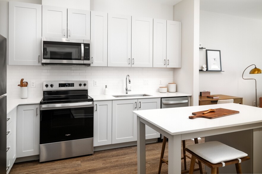 New West Phase apartments - Finish Package III Kitchen with stainless steel appliances, white quartz countertops, grey cabinetry, pendant lighting, and hard surface flooring - Avalon Hunt Valley and Hunt Valley West