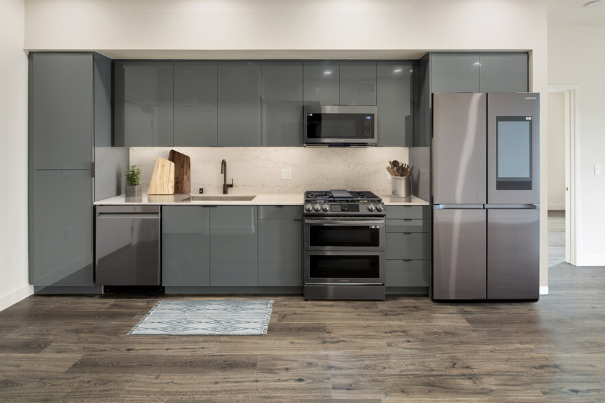 Upgrade Package Kitchen with grey cabinetry, undercabinet lighting, marble backsplash and countertop, and black stainless steel appliances - AVA Arts District