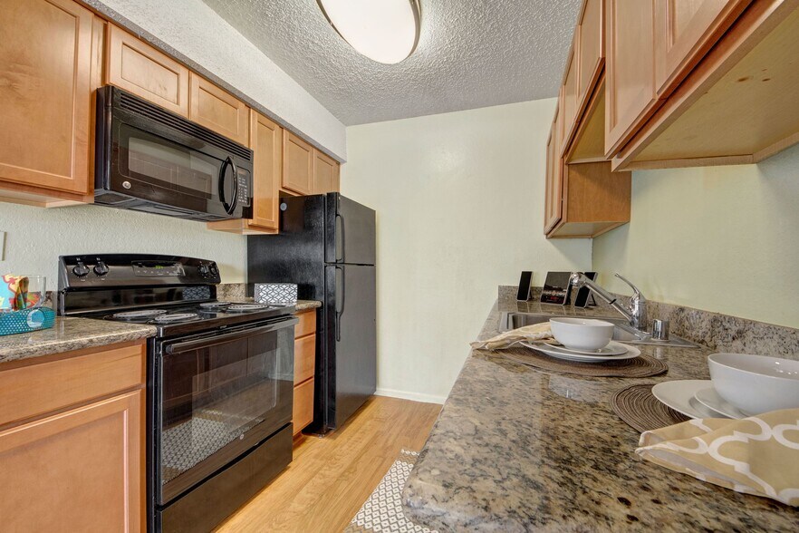 A kitchen with granite countertops, cabinet storage, and sleek black appliances - Avalon Springs