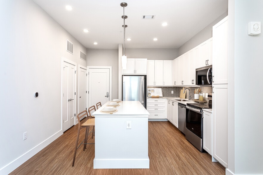 Modern kitchen with white cabinetry, undercabinet lighting, grey tile backsplash, and white quartz countertops - Avalon Carmel Commons
