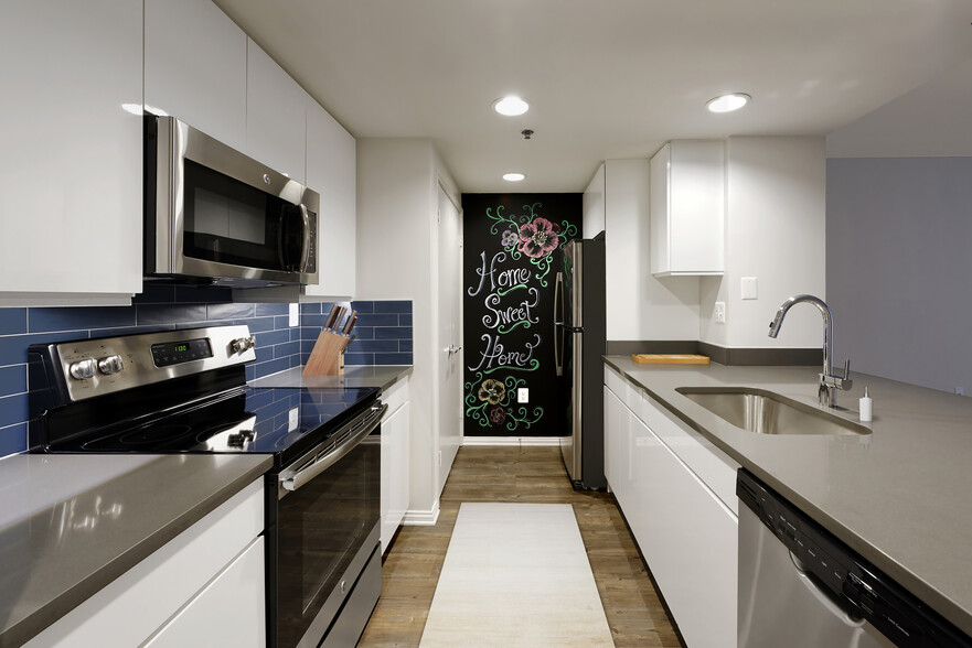 Renovated Package III kitchen with grey quartz countertops, blue tile backsplash, white cabinetry, stainless steel appliances, and hard surface plank flooring - AVA Ballston Square