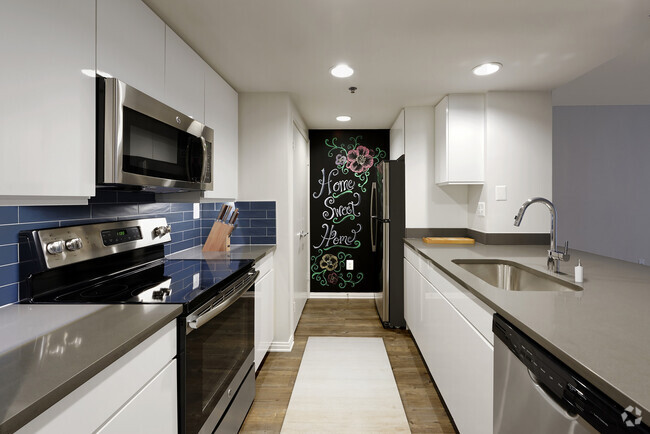 Renovated Package III kitchen with grey quartz countertops, blue tile backsplash, white cabinetry, stainless steel appliances, and hard surface plank flooring - AVA Ballston Square