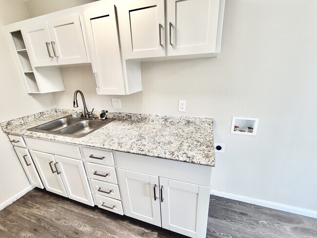 Modern kitchen with sleek white cabinets, elegant granite countertops, and a double stainless steel sink. - 8867 W 54th