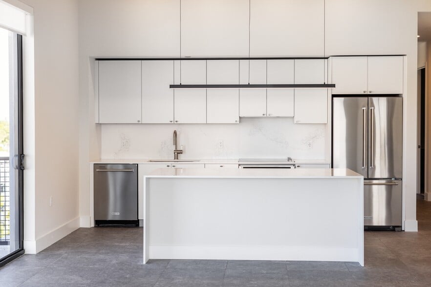 Signature Collection kitchen with white cabinetry, white marbled quartz countertop and backsplash, wine fridge, and upgraded stainless steel appliances - Avalon South Miami