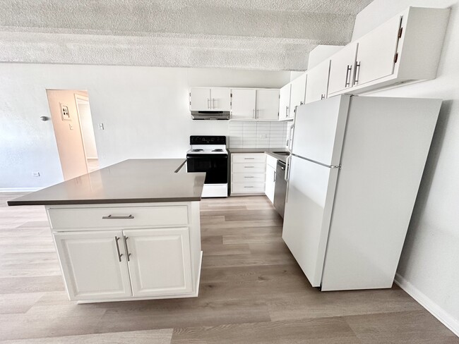 Bright, modern kitchen with sleek white cabinetry, spacious island, and contemporary appliances. - Columbine Plaza