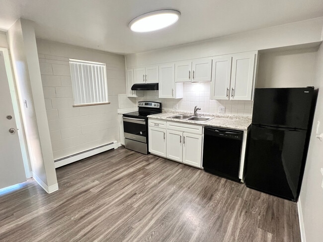 Modern kitchen with sleek white cabinetry, granite countertops, and stainless steel appliances, accented by elegant dark flooring. - Lakeview Apartments
