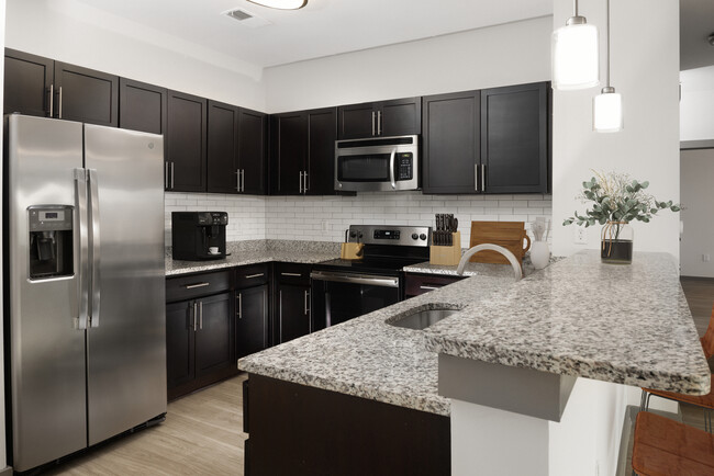 Renovated Package II Kitchen with dark cabinetry, speckled granite countertops, white tile backsplash, stainless steel appliances, pendant lighting, and hard surface flooring - AVA South End