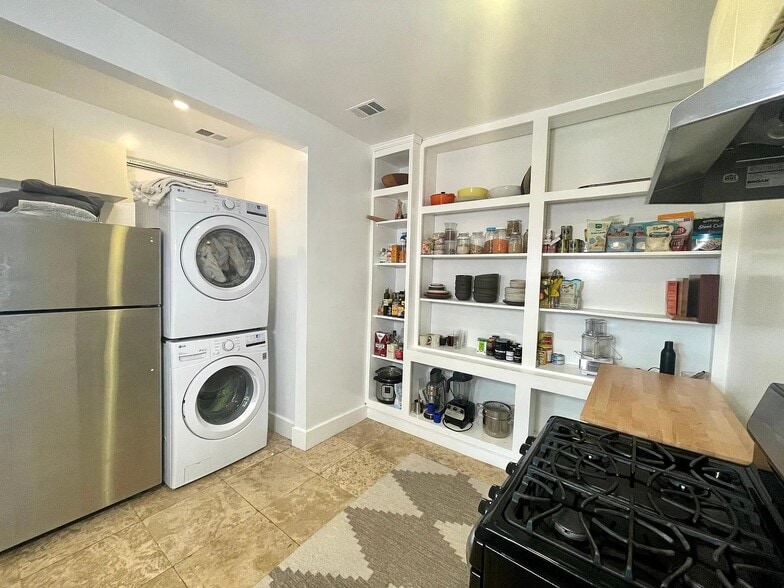 Kitchen includes a full-size refrigerator, stacked washer and dryer, and open shelving. - 6000 Carlton Way