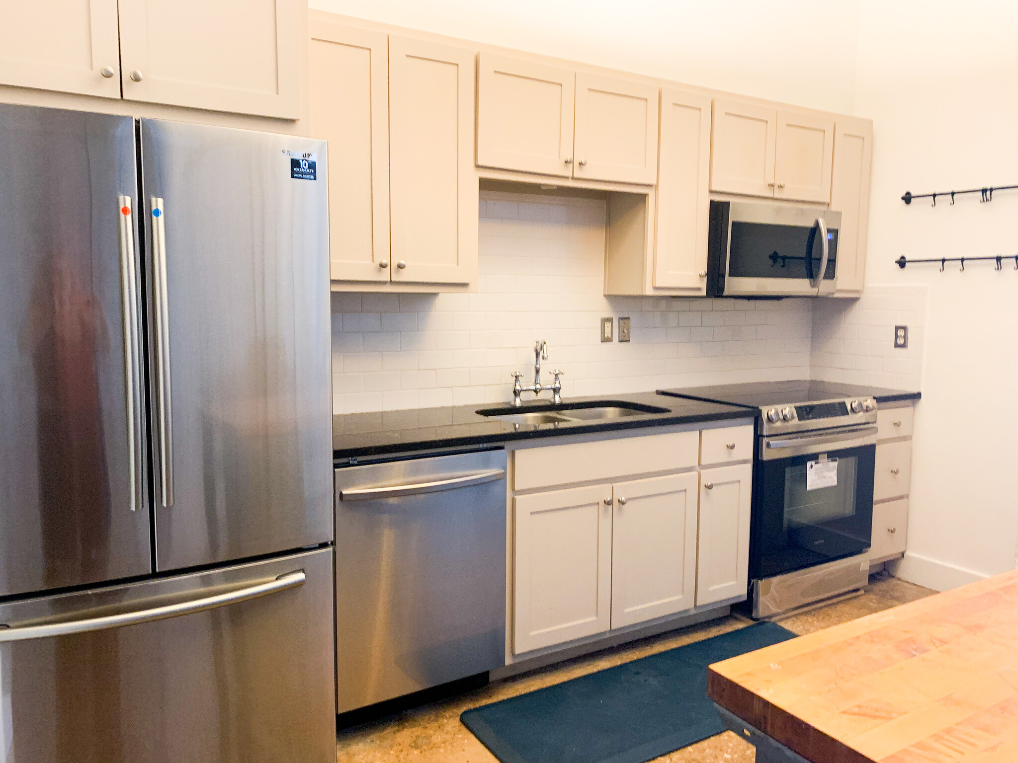 Galley style kitchen features brand-new Samsung stainless appliances, granite countertops, white subway tiles, task lighting under cabinets, flat top electric stove, mounted microwave, dishwasher, side by side refrigerator, and garbage disposal. - 659 Auburn Ave NE #145