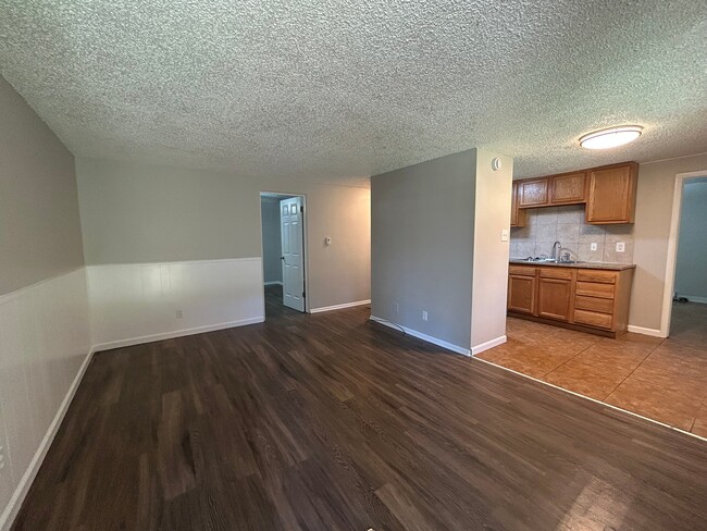Cozy apartment interior featuring an open living area with elegant wood flooring, adjacent to a compact kitchen with warm wooden cabinetry. - Boardwalk Apartments