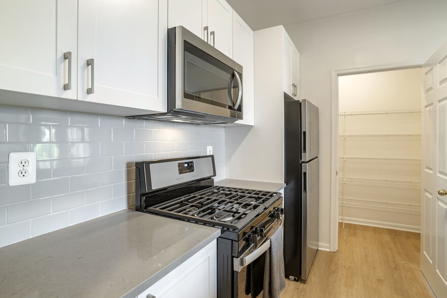 Renovated Package II kitchen with white cabinetry, grey quartz countertops, tile backsplash, stainless steel appliances, and hard surface flooring - Avalon Reston Landing