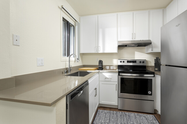 Renovated I kitchen with grey quartz countertops, white cabinetry, stainless steel appliances, and hard surface flooring - eaves Warner Center