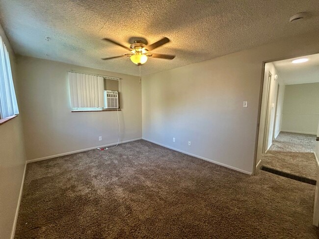 Cozy bedroom with plush carpeting, ceiling fan, and natural light from a window air conditioner unit. - Boardwalk Apartments