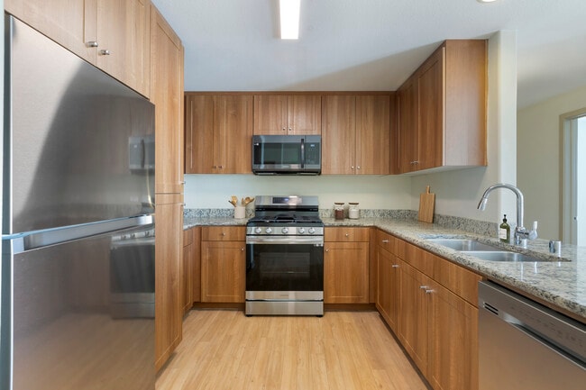 Renovated Package I kitchen with oak cabinetry, beige speckled granite countertops, stainless steel appliances, and hard surface flooring - Avalon San Dimas