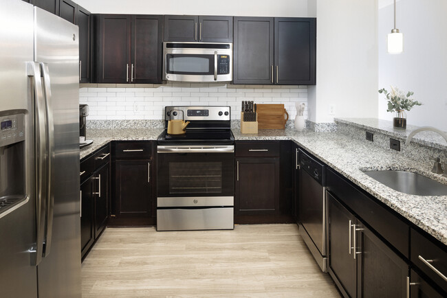 Renovated Package II Kitchen with dark cabinetry, speckled granite countertops, white tile backsplash, stainless steel appliances, pendant lighting, and hard surface flooring - AVA South End