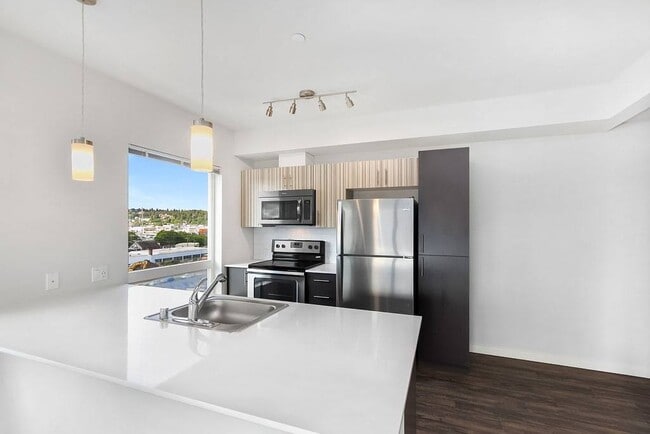 A bright, open kitchen with stainless steel appliances, a large window overlooking Ballard, and lots of counter space - Vive