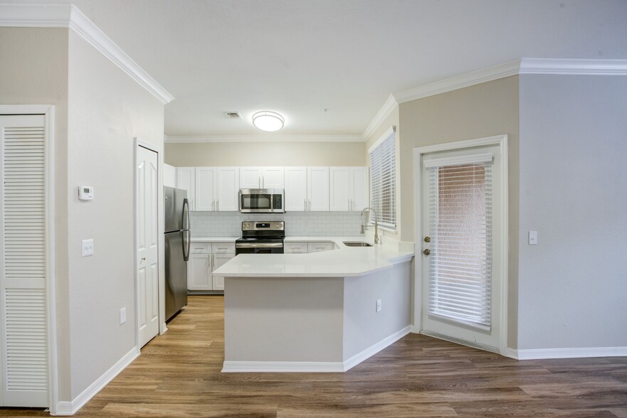 Living room and kitchen with island, wood-style plank flooring, and crown molding. - Amara at Metro West