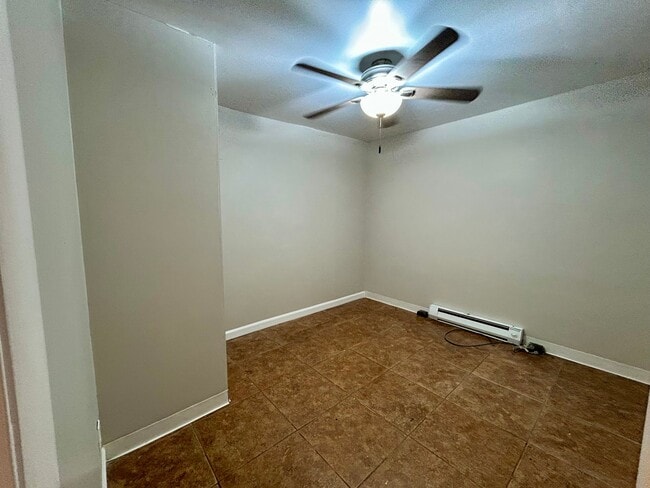 Cozy room with sleek tiled flooring, neutral walls, and a modern ceiling fan, perfect for versatile living. - Boardwalk Apartments