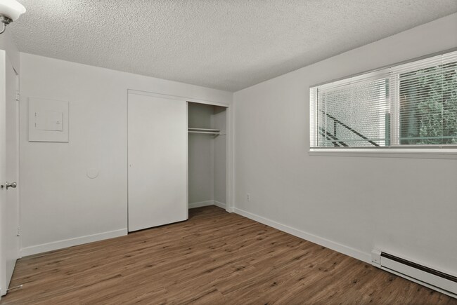 Cozy bedroom with modern flooring and ample closet space. - Rainier Gardens Aparments