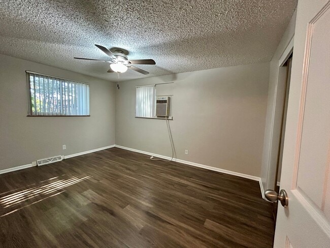 Bright and inviting room with sleek hardwood flooring, a ceiling fan for comfort, and natural light filtering through large windows. - Boardwalk Apartments