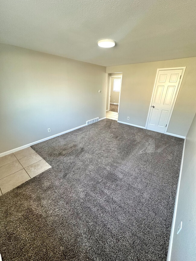 Bright and inviting room with fresh carpet, neutral toned walls, and a modern light fixture, perfect for a cozy living space. - 7750-7766 West 39th Ave
