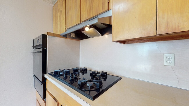Explore this chic kitchen space featuring a stylish gas stove and ample wooden cabinetry. - Flats at Sloan's Lake West