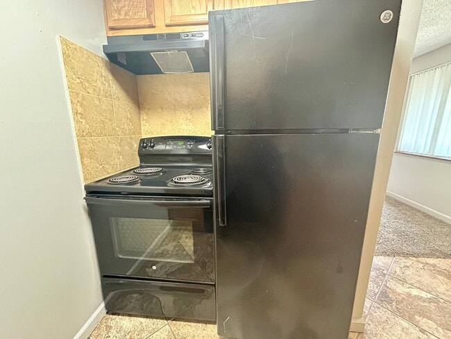 Modern kitchen featuring a sleek black refrigerator and stove with elegant tiled backsplash, offering a stylish and functional cooking space. - Boardwalk Apartments