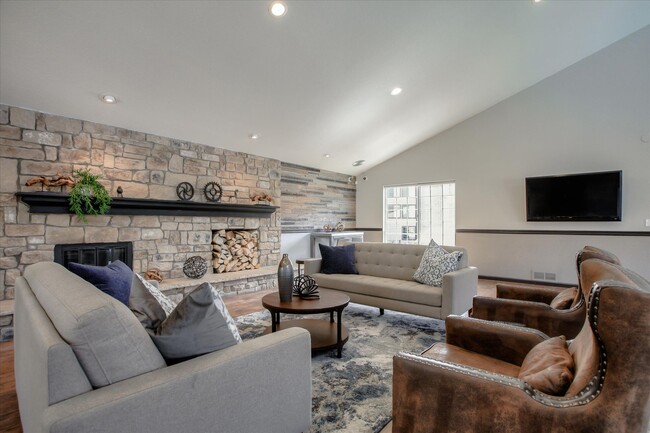 Image of the resident club house with couches, a table, a stone wall, a fireplace, and a television. - Chestnut Ridge Apartment Homes