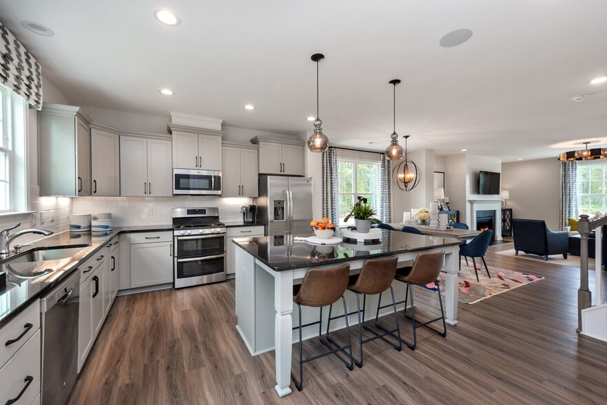 Kitchen with light grey cabinetry, black granite countertops. white tile backsplash, stainless steel appliances, and hard surface flooring - Avalon Townhomes Brier Creek
