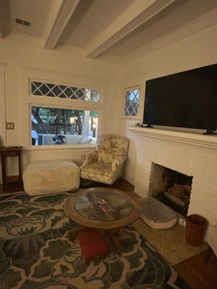 Cozy living area with original windows, white brick fireplace, and hardwood floors. - 6000 Carlton Way