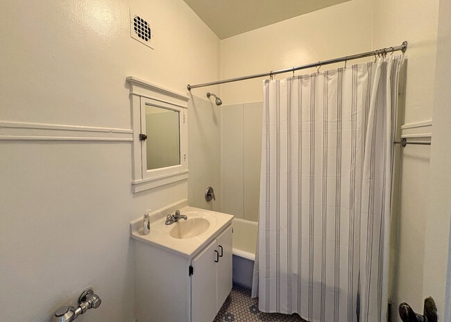 Bright and clean bathroom with classic white fixtures, featuring a mirrored vanity, shower, and elegant tile flooring. - Ivanhoe