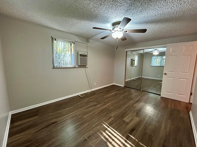 Spacious bedroom featuring sleek hardwood floors, mirrored closet doors, and a ceiling fan for enhanced comfort. - Boardwalk Apartments