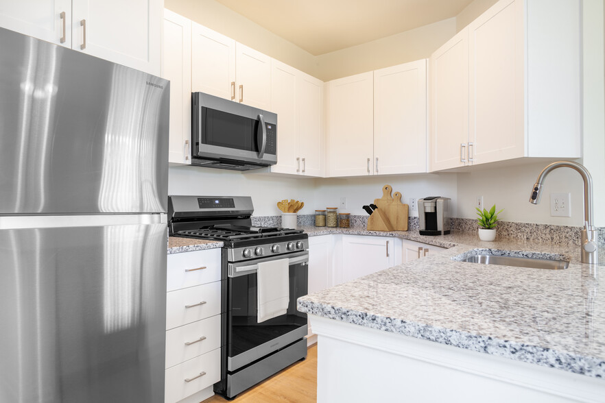 Renovated Package I kitchen with white cabinetry, grey granite countertops, stainless steel appliances, and hard surface plank flooring - Avalon Russett