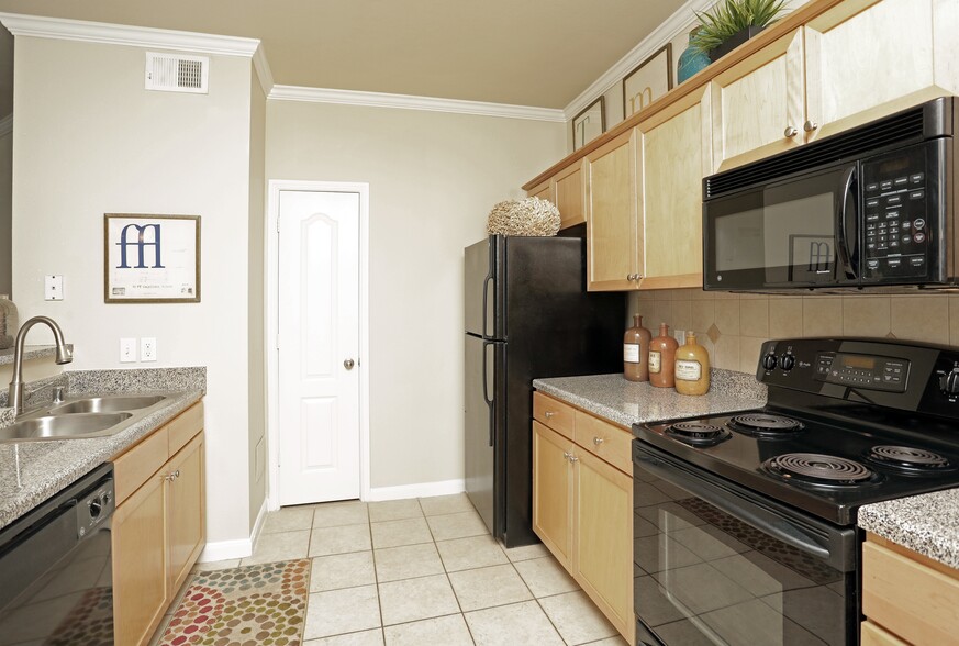 Kitchen with oak cabinetry, speckled granite countertops, black appliances, and hard surface flooring - eaves Twin Creeks