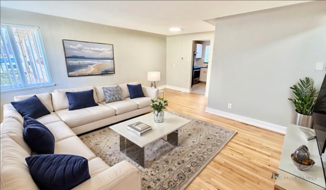 Bright and modern living room with elegant light wood flooring, accentuated by natural light from the window. - Flats at 16th
