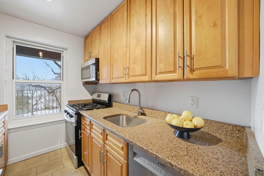 Kitchen featuring stainless steel appliances, wood cabinetry and light stone countertops - 555 Broadway