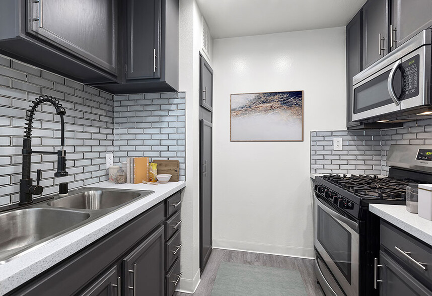 White tiled kitchen with stainless steel fridge, oven, microwave, and fixtures. - Chateau Encino