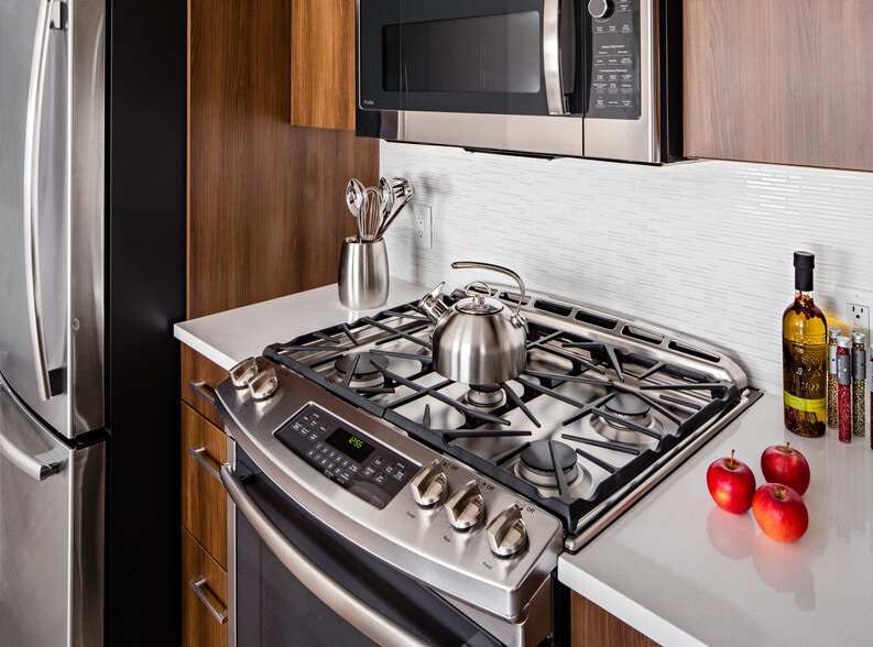 Signature Collection Kitchen with oak cabinetry, light grey quartz countertops, white tile backsplash, upgraded stainless steel appliances, and hard surface plank flooring - Avalon Princeton