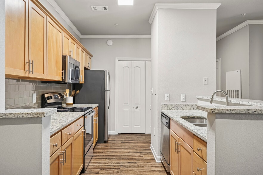 Kitchen with oak cabinetry, speckled granite countertops, stainless steel appliances, and hard surface flooring - eaves Twin Creeks