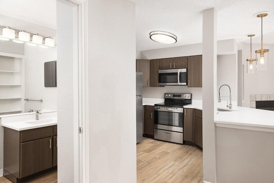 Modern apartment kitchen with elegant white countertops, stainless steel appliances, and warm wood flooring. - Avana Belmar