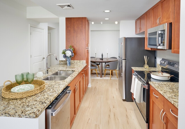Newly Renovated Ellington Floor Plan Kitchen at Meridian at Grosvenor Station featuring sleek stainless steel appliances, modern vinyl plank wood-style flooring, and updated lighting fixtures that complement existing granite countertops and custom cabinetry. - Meridian at Grosvenor Station