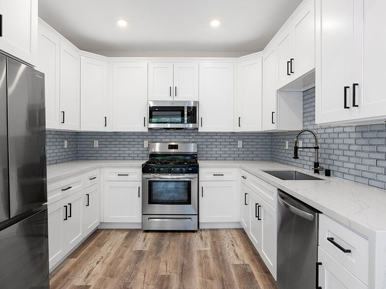 White tiled kitchen with stainless steel fridge, over, microwave, and fixtures. - Palms Court