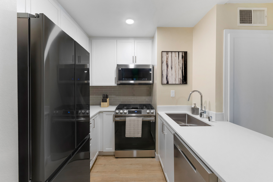 Renovated Package I kitchen with stainless steel appliances, white quartz countertops, white cabinetry, grey tile backsplash, and hard surface flooring - Avalon Burbank