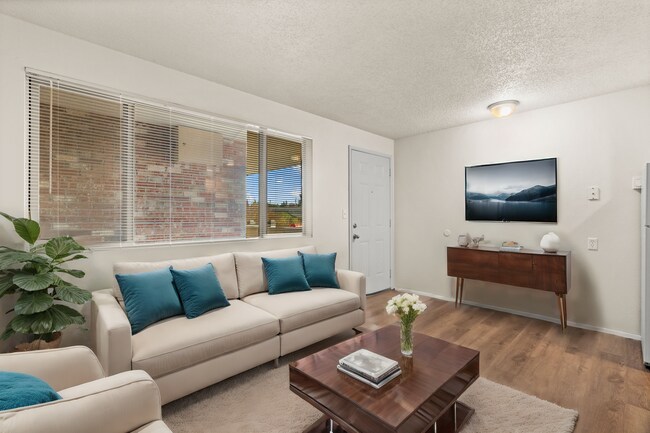 Bright and stylish living room, virtually staged to highlight cozy seating, modern décor, and warm wood-style flooring. - Highland Court Apartments