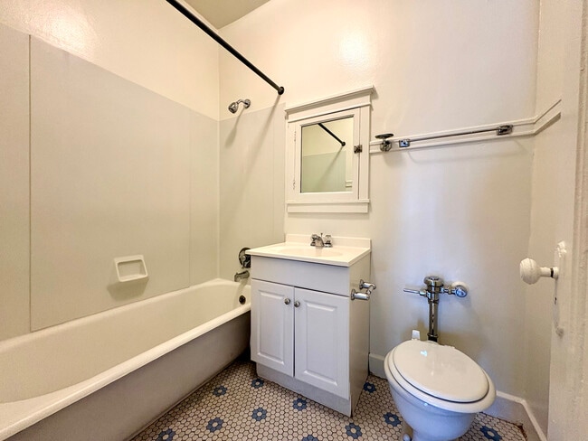 Bright bathroom with classic white fixtures, featuring a bathtub, elegant hexagonal tile flooring, and a stylish vanity with a mirrored cabinet. - Ivanhoe