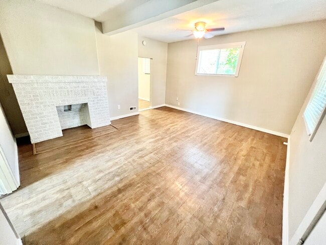 Experience the warmth of a cozy living room with a charming brick fireplace and modern ceiling fan. - Barnum Park